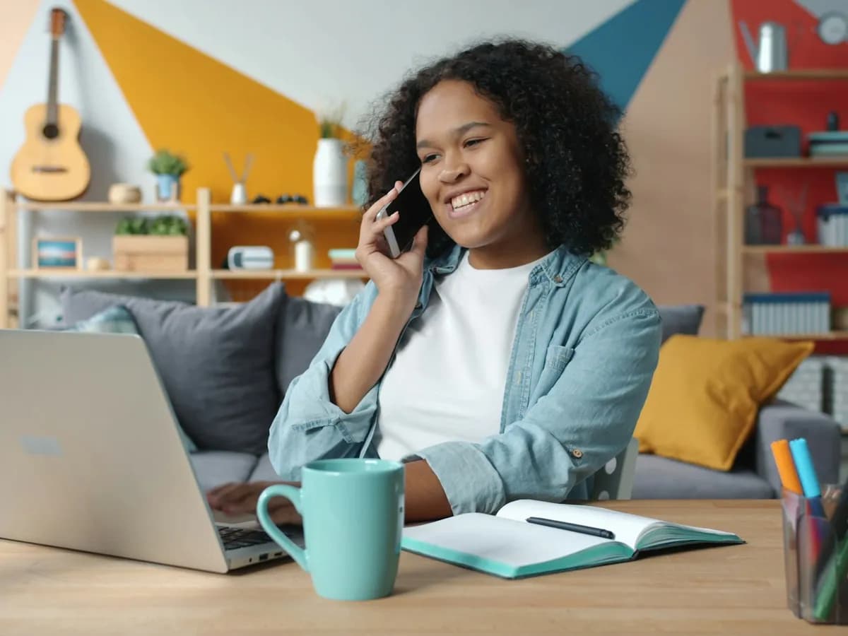Woman on the phone at her desk with a laptop and an open notebook