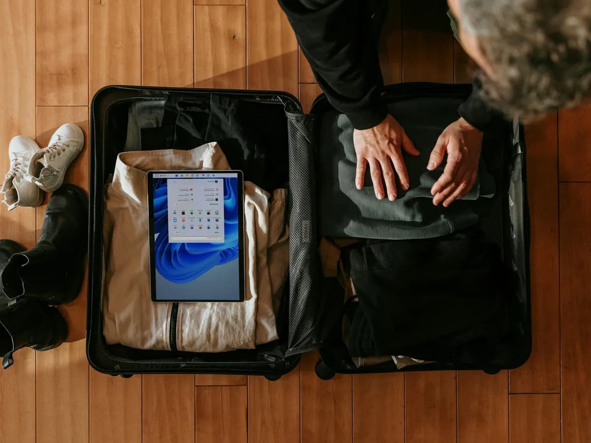 Someone packing clothes and a tablet into a suitcase